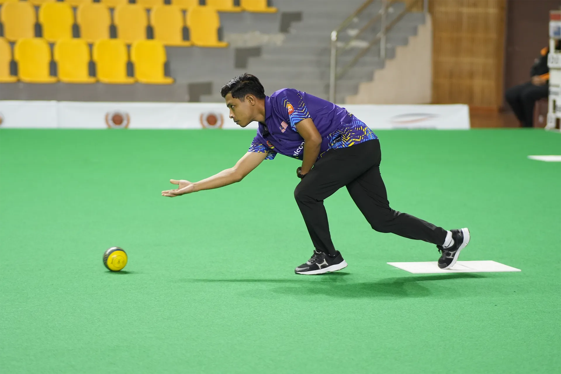 Malaysian lawn bowls athlete delivering a bowl on an indoor green