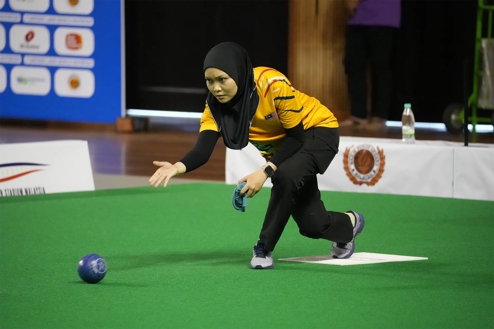 Malaysian lawn bowls athlete delivering a bowl during competition
