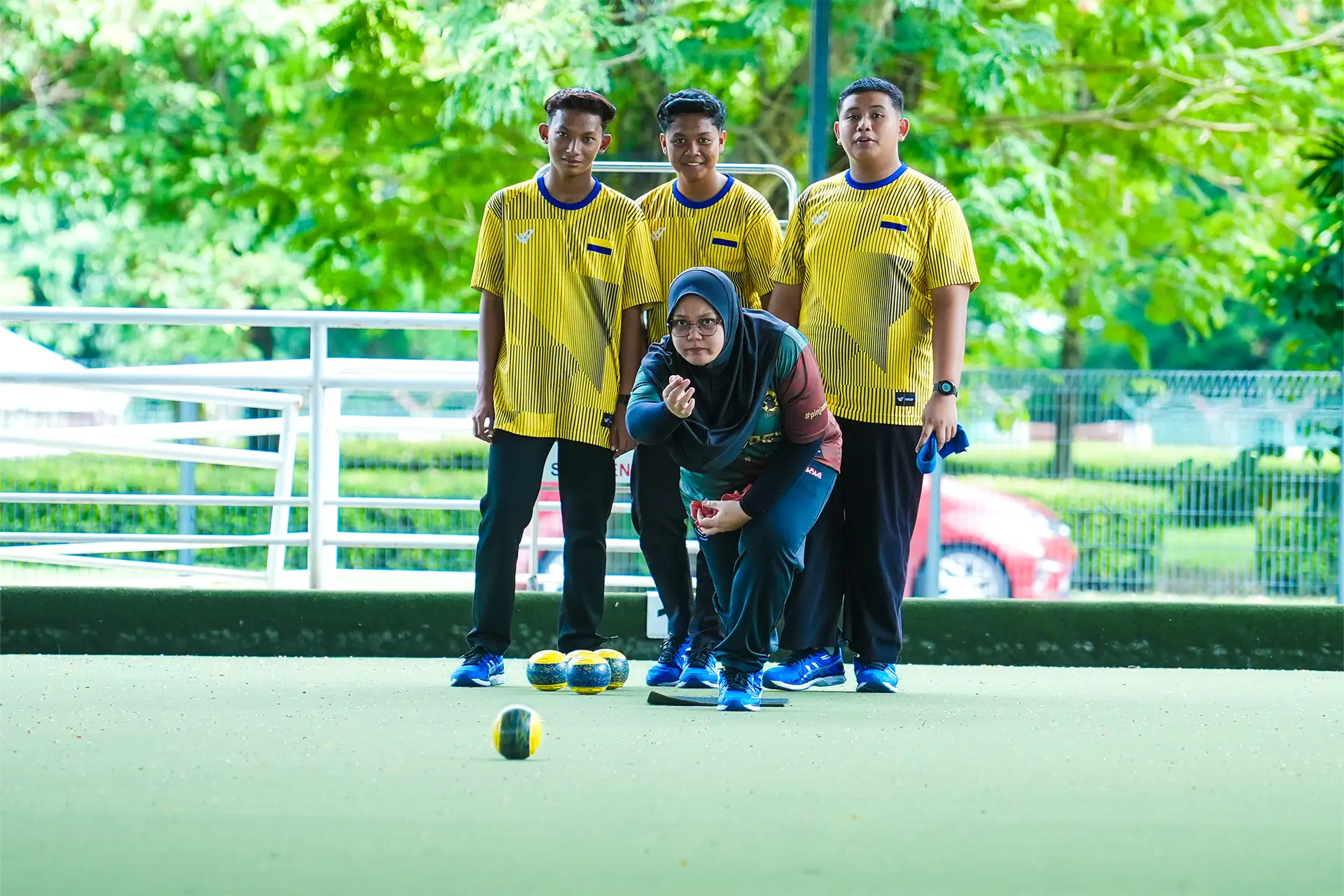 Young lawn bowls players with an athlete delivering a bowl